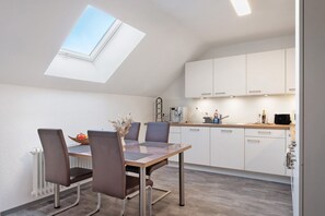 Une cuisine moderne dotée d’une verrière, de meubles blancs et d’un coin repas avec une table et des chaises.