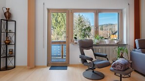 A modern living room with a sliding glass door leading to a balcony, a grey armchair, a small table, and a radiator. - Apartment 'Kessler Waldblick' with Balcony and Wi-Fi (Häusern)