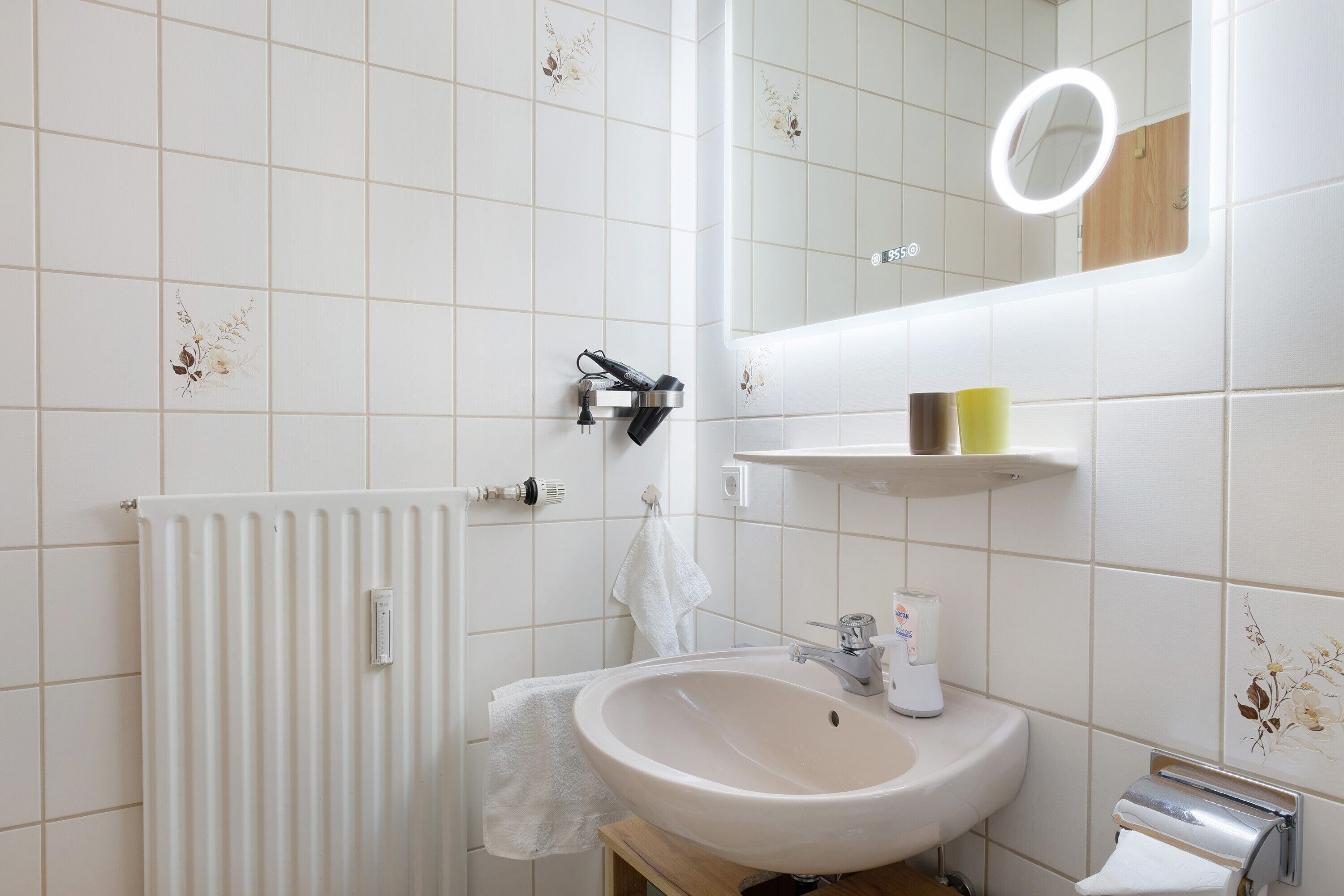 Ein Badezimmer mit Waschbecken, Spiegel, Handtuchhalter und Heizkörper.