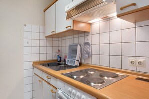 A kitchen with white tiles, a stove, an oven, a sink, and a dish rack.