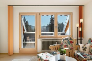 A room with a large window, a radiator, a chair, a sofa, and a lamp.
