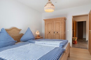A bedroom with a bed, a wooden wardrobe, a nightstand with a lamp, and a door leading to another room.
