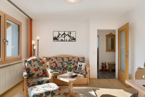 A living room with a sofa, chairs, a small table, a radiator, a wall art piece, a mirror, and a door.