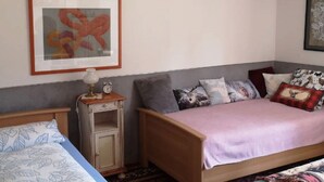 A bedroom with two beds, a bedside table with a lamp, and a framed artwork on the wall.