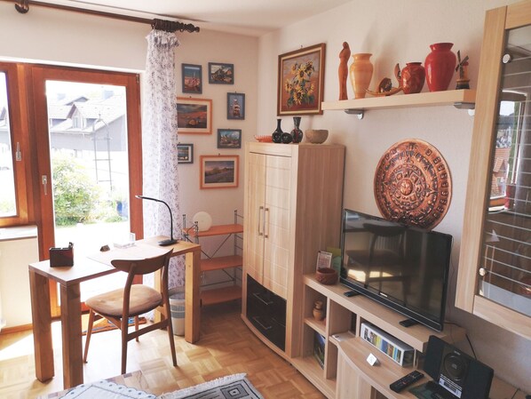 A living room with a television, wooden furniture, a cabinet, and various wall decorations.