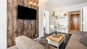 Un salon moderne avec un téléviseur à écran plat fixé à un mur en bois, un canapé, une table basse et un coin repas comprenant des chaises et une petite table.