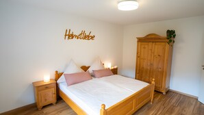 Ein Schlafzimmer mit einem hölzernen Bett, Nachttischen, einem Kleiderschrank und einer Wand mit dem Schriftzug 'Heimlichkeit'.