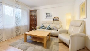 A living room with a sofa, a coffee table, a bookshelf, and a window with sheer curtains. - Apartment 'Thum' with Private Terrace and Wi-Fi (Daisendorf)