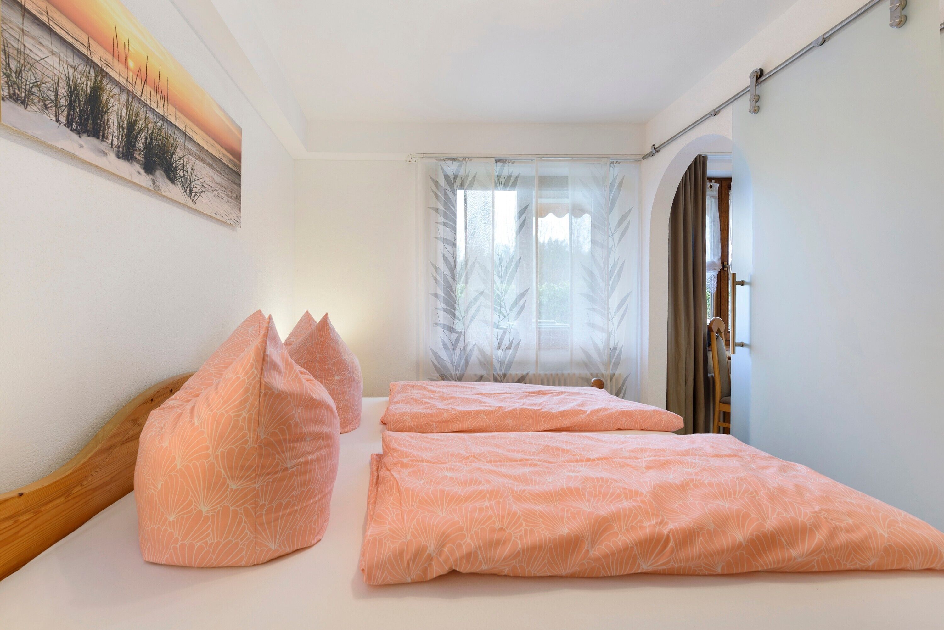 Quarto com uma cama, almofadas, janela com cortinas e um quadro na parede.