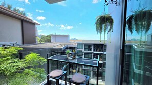 A modern balcony with a glass table and chairs, a hanging plant, and a view of neighboring buildings. - Room-a301- 1 Bedroom Corner Condo Forest (Krabi)