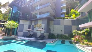 A modern building with a swimming pool, lounge chairs, and umbrellas. - Room-a301- 1 Bedroom Corner Condo Forest (Krabi)