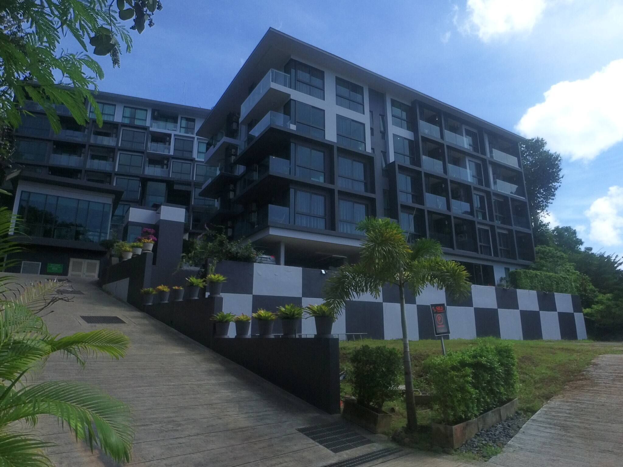 A modern multi-story building with balconies, a checkered wall design, and potted plants.