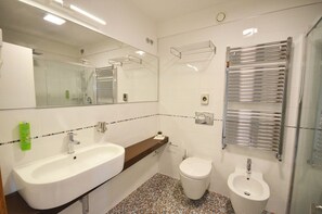 Un baño moderno con un lavabo blanco, un inodoro y un bidé. Hay un espejo sobre el lavabo y un perchero en la pared.