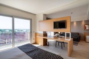 Un dormitorio moderno con una cama grande, un escritorio con televisor y un balcón con vistas.