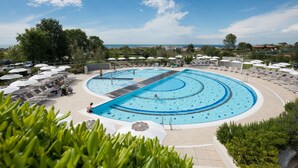 Una gran piscina al aire libre con múltiples carriles, rodeada de tumbonas y sombrillas, y vista al mar de fondo.