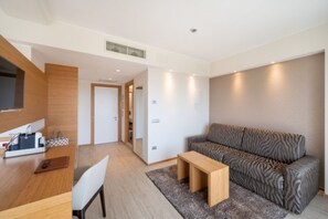 Ein modernes Wohnzimmer mit einer Couch, einem Couchtisch und einem Schreibtisch mit Stuhl. Eine Tür führt in einen weiteren Raum.