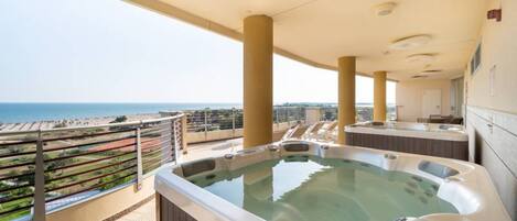 A rooftop terrace with a hot tub, a view of the sea, and a bar area.