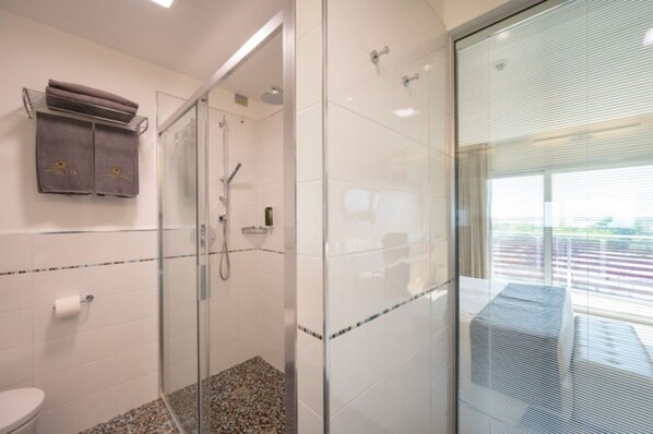 Un baño moderno con cabina de ducha de vidrio, inodoro y toallero con dos toallas.