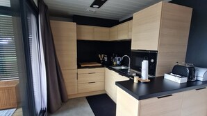 A compact kitchen with wooden cabinets, a black countertop, and a microwave. - Agde Prestige Chalet in private residence with Pools and Spa (Agde)