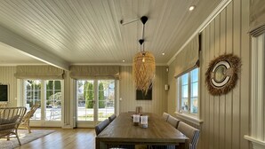 A dining area with a wooden table and chairs, a hanging light fixture, and a view through large glass doors. - Premium Villa included Boat, Golf Cart & Sea View, Kragerø SPA Resort vicinity (Kragerø)
