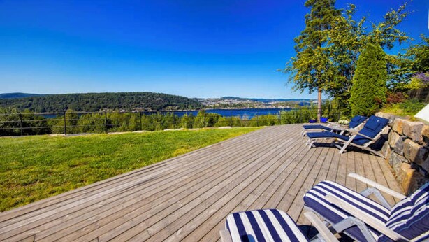 A wooden deck with lounge chairs overlooking a lake and hills. - Premium Villa included Boat, Golf Cart & Sea View, Kragerø SPA Resort vicinity (Kragerø)