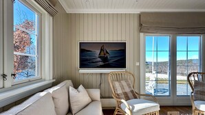 A living room with a sofa, two wicker chairs, a flat-screen TV, and a large window with a scenic view. - Premium Villa included Boat, Golf Cart & Sea View, Kragerø SPA Resort vicinity (Kragerø)