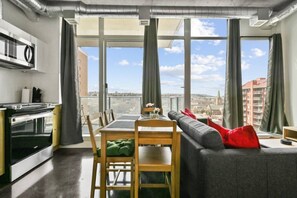 A modern apartment with a dining area, kitchen, and large windows offering a city view. - Bright Studio | Mins to Saddledome | Skyline Views (Calgary)