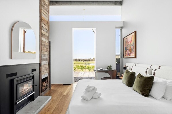 Une chambre moderne avec une cheminée, un grand lit avec des oreillers, un bureau et une vue sur l’extérieur.