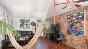 Una sala de estar con una hamaca, un sofá, un televisor, una chimenea y una pared de piedra con obras de arte.