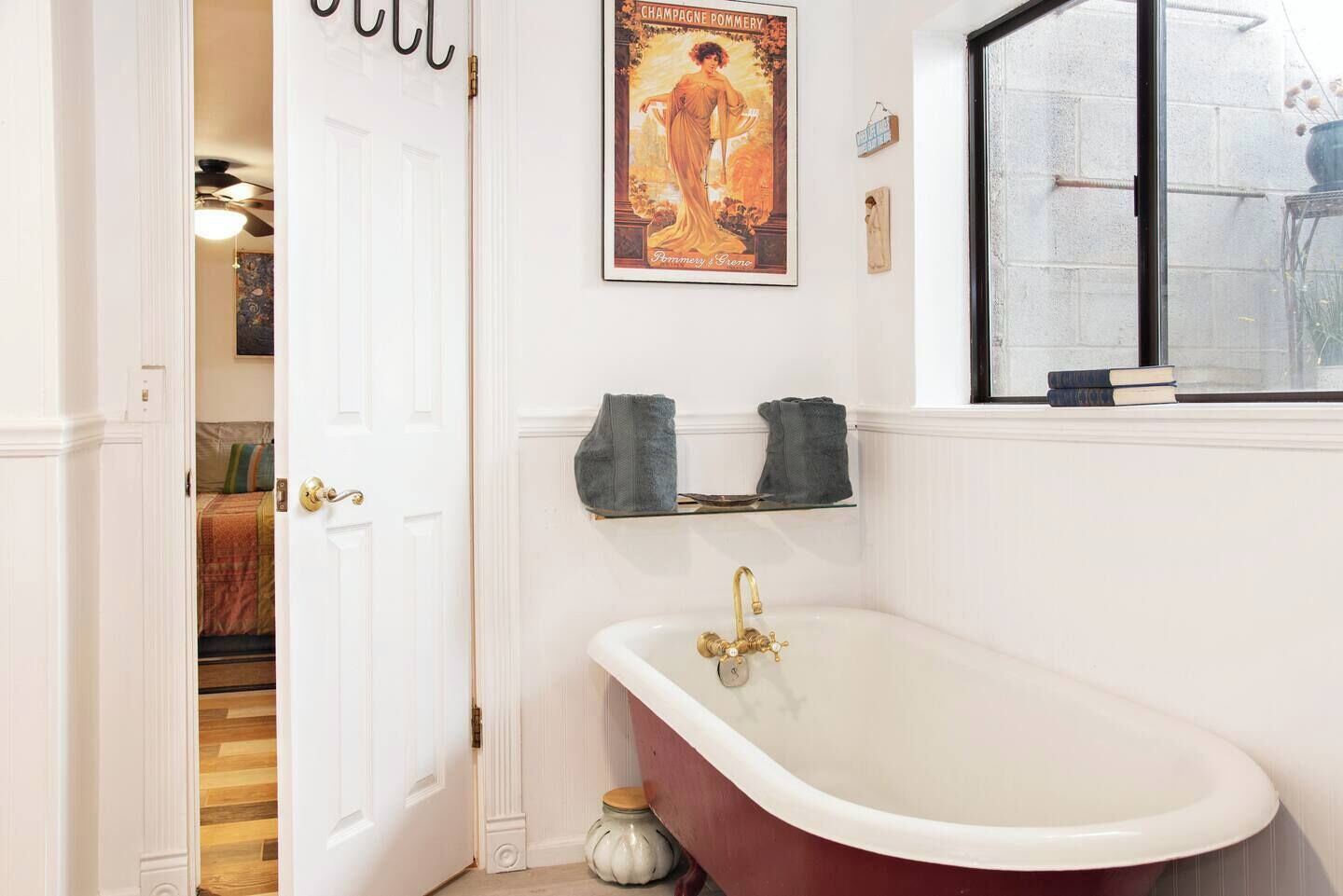 Une salle de bain avec une baignoire blanche, une affiche accrochée au mur et une fenêtre dont l’encadrement est garni de livres.