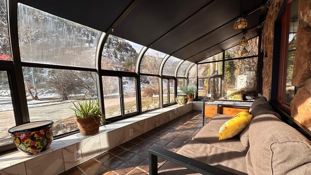 Un rincón acogedor para leer con un banco acolchado, una planta en maceta y un asiento junto a la ventana con vistas a un paisaje nevado.