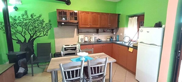 Uma cozinha compacta com armários de madeira, uma mesa de jantar com cadeiras, um refrigerador e uma pequena ilha com pia.