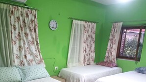 Ein Zimmer mit zwei Betten, grünen Wänden, blumigen Vorhängen, einer Uhr und einem Fenster mit Jalousien.