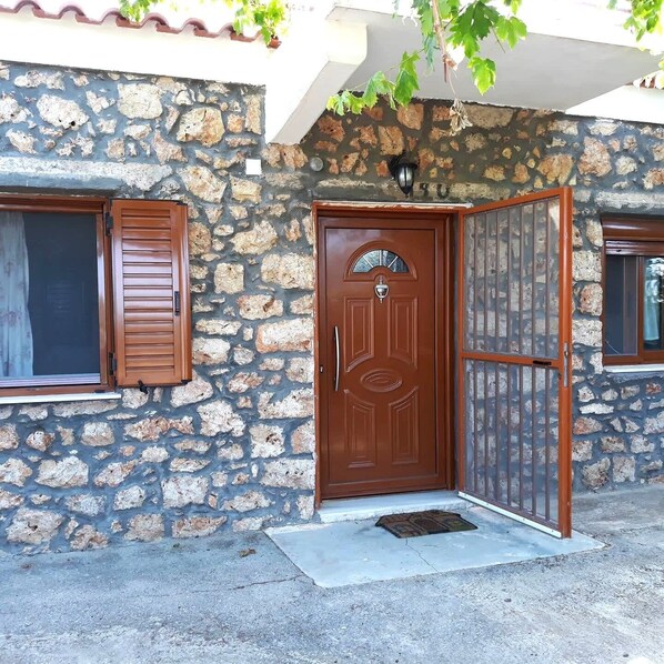 A stone building with a brown door, a window with shutters, and a small porch area.