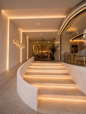 A modern hotel interior with a curved staircase, a reception area, and a seating area with a view. - Aspira Central Patong (Patong)