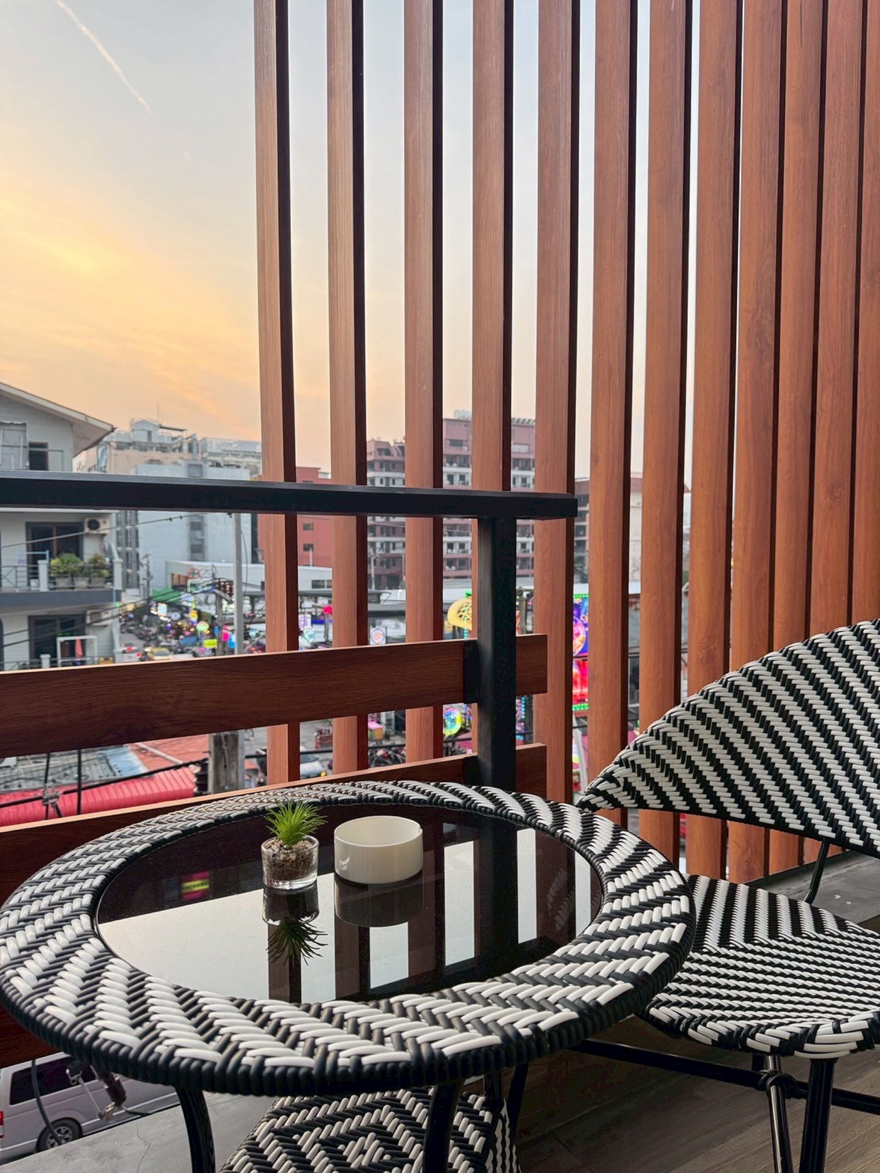 A balcony with a wooden partition, a round table with a woven chair, and a small potted plant.