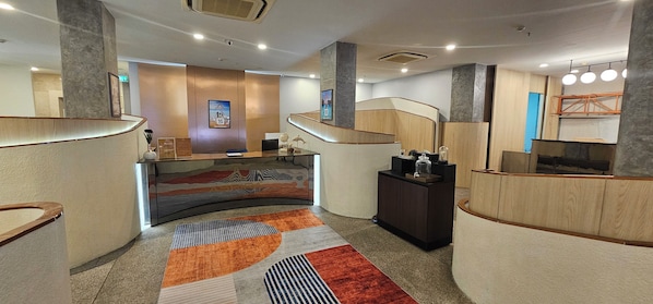 Un moderno vestíbulo de hotel con un mostrador de recepción curvo, una escalera y una alfombra estampada.