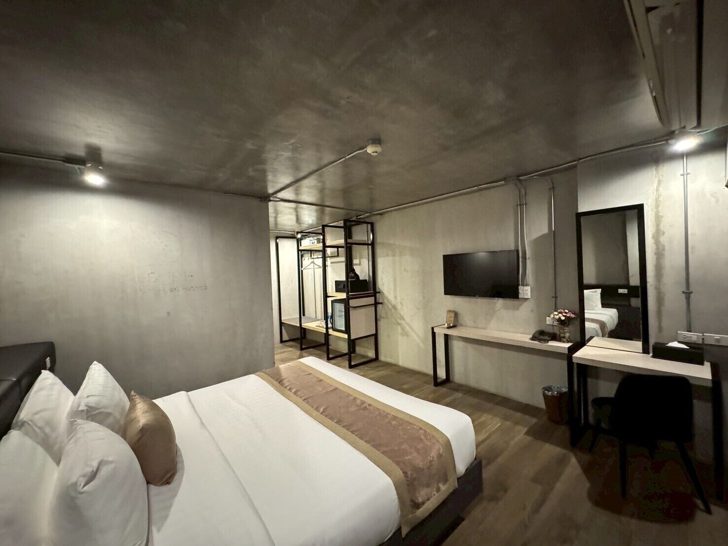 A modern hotel room with a bed, a desk, a TV, and a mirror.