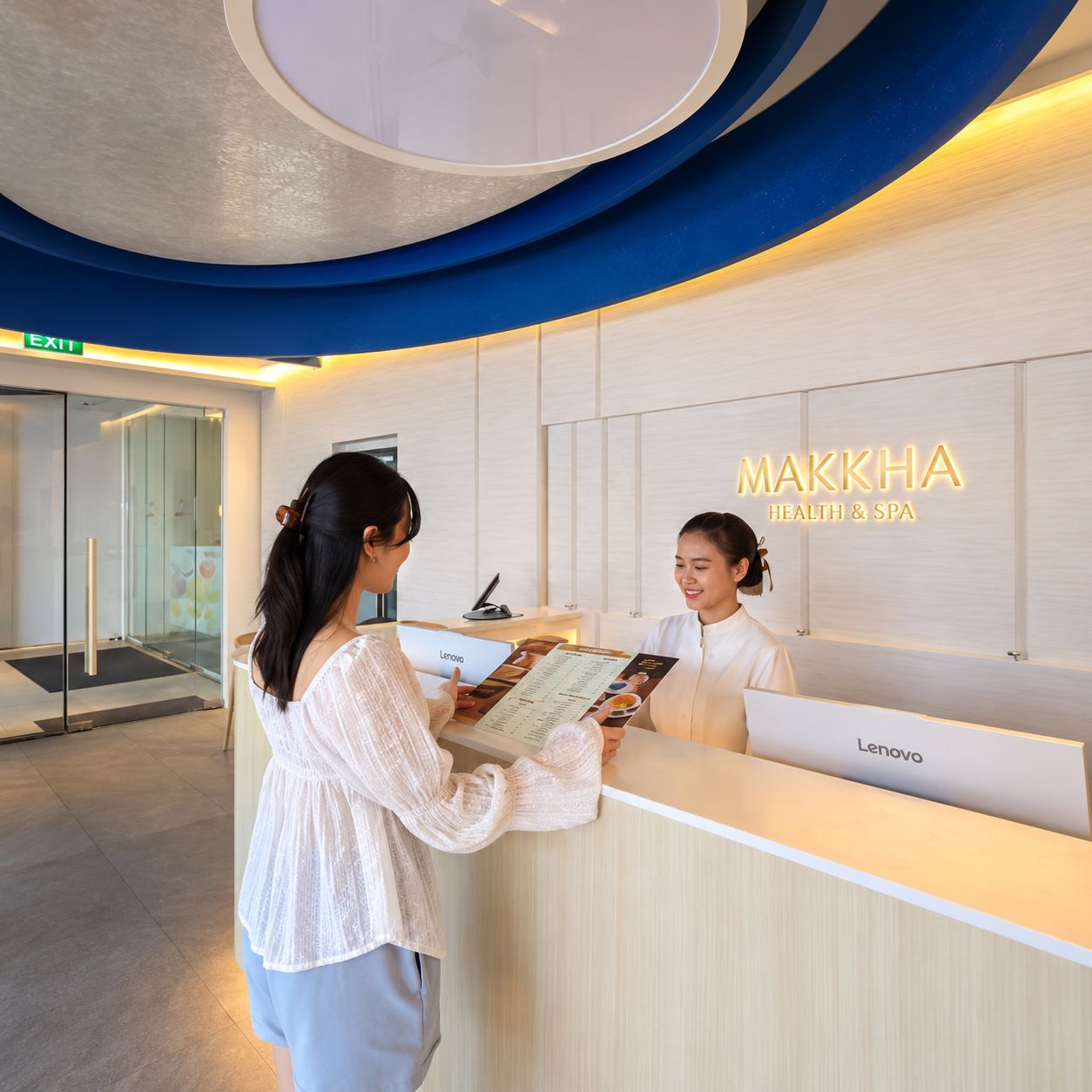 Un comptoir d’accueil avec une enseigne indiquant « MAKKHA Health & Spa » et le nom de marque Lenovo.
