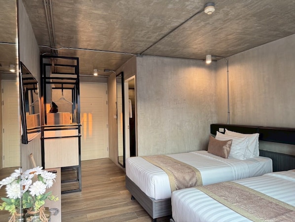 A modern hotel room with two beds, a wooden floor, a concrete ceiling, and a large mirror.