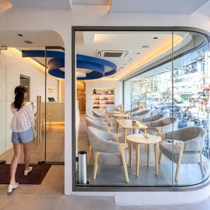 A modern interior with a reception desk, seating area, and a view of the street. - Aspira Central Patong (Patong)