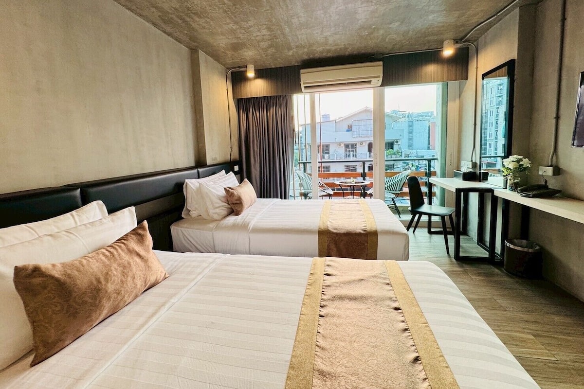 Habitación de hotel con dos camas, un balcón con mesa y sillas, y vista a la ciudad.