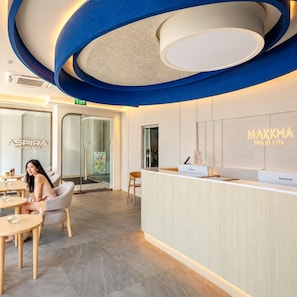 A modern reception area with a reception desk, a treatment room labeled 'ASPIRA,' and a sign for 'MAKKHA HEALTH & SPA.' - Aspira Central Patong (Patong)