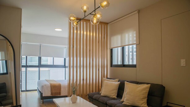 A modern living room with a sofa, a coffee table, and a bed with a window view. - w* | Modern 1BR in San Isidro (Lima)