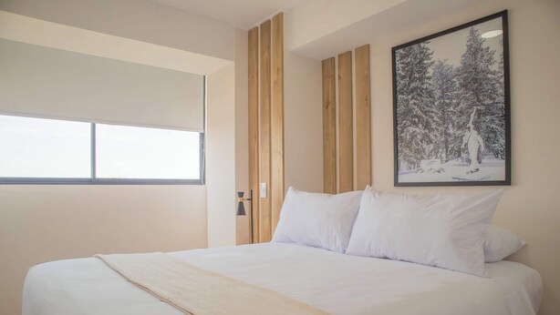 A bedroom with a large bed, a window with blinds, a framed picture on the wall, and wooden paneling.