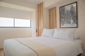 Une chambre avec un grand lit, une fenêtre avec des stores, un tableau encadré au mur et un lambris en bois.