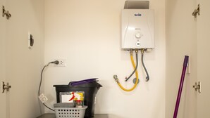 A compact laundry room with a front-loading washing machine, a wall-mounted water heater, and a mop and bucket.