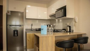 A modern kitchen with a stainless steel refrigerator, a microwave, a coffee maker, and a bar area with stools.