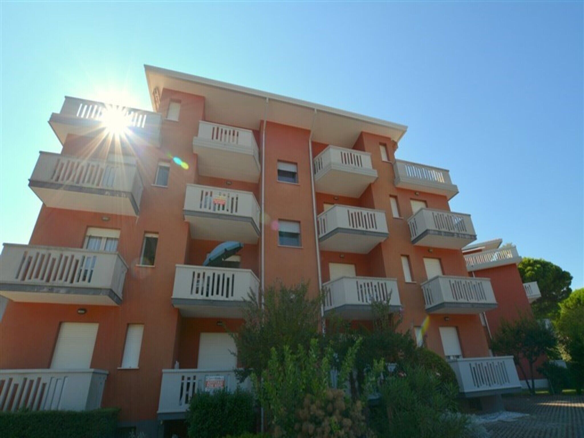 A multi-story residential building with balconies, a central stairwell, and a clear sky.