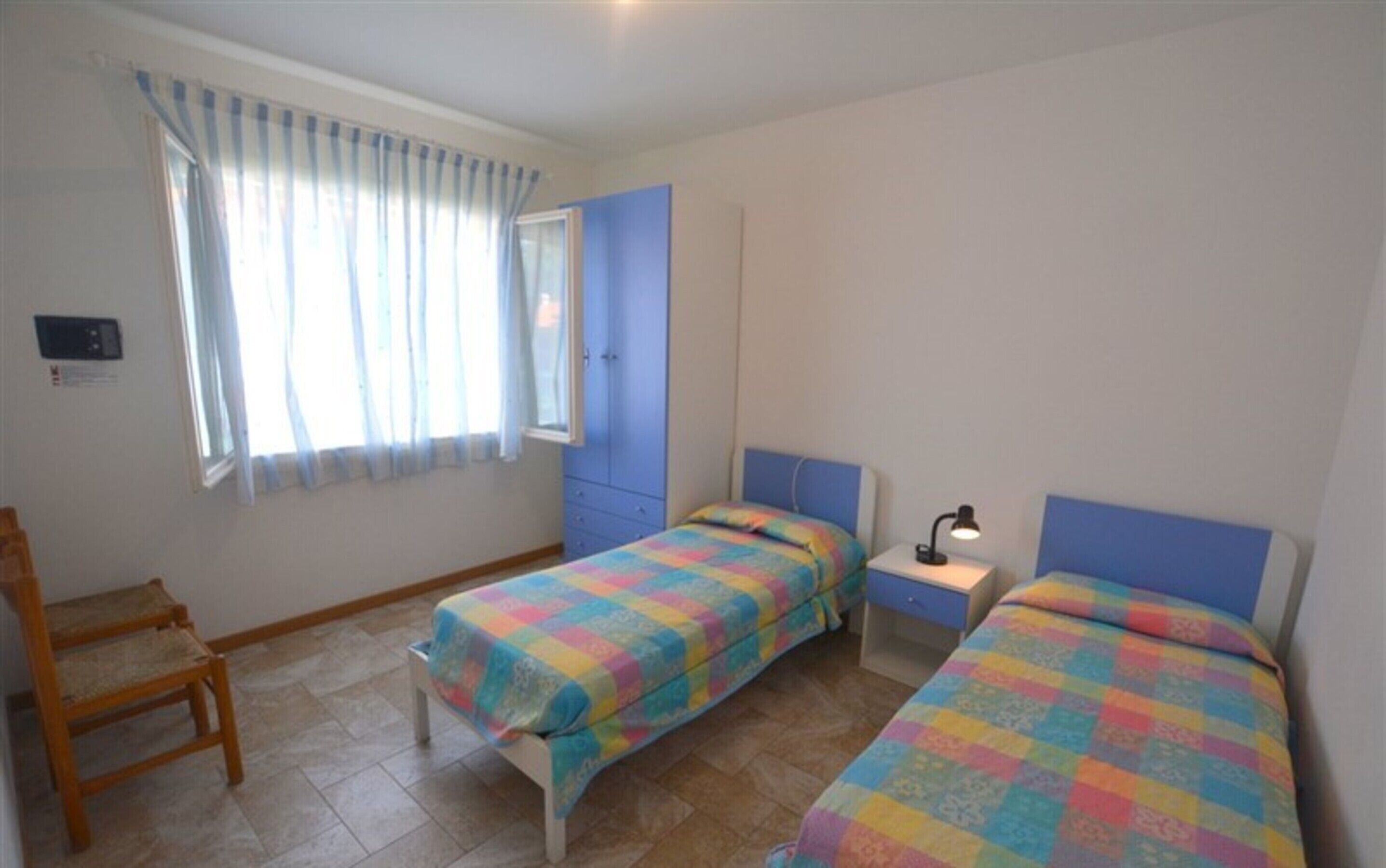 Une chambre avec deux lits, une chaise, un bureau et une fenêtre avec des rideaux.